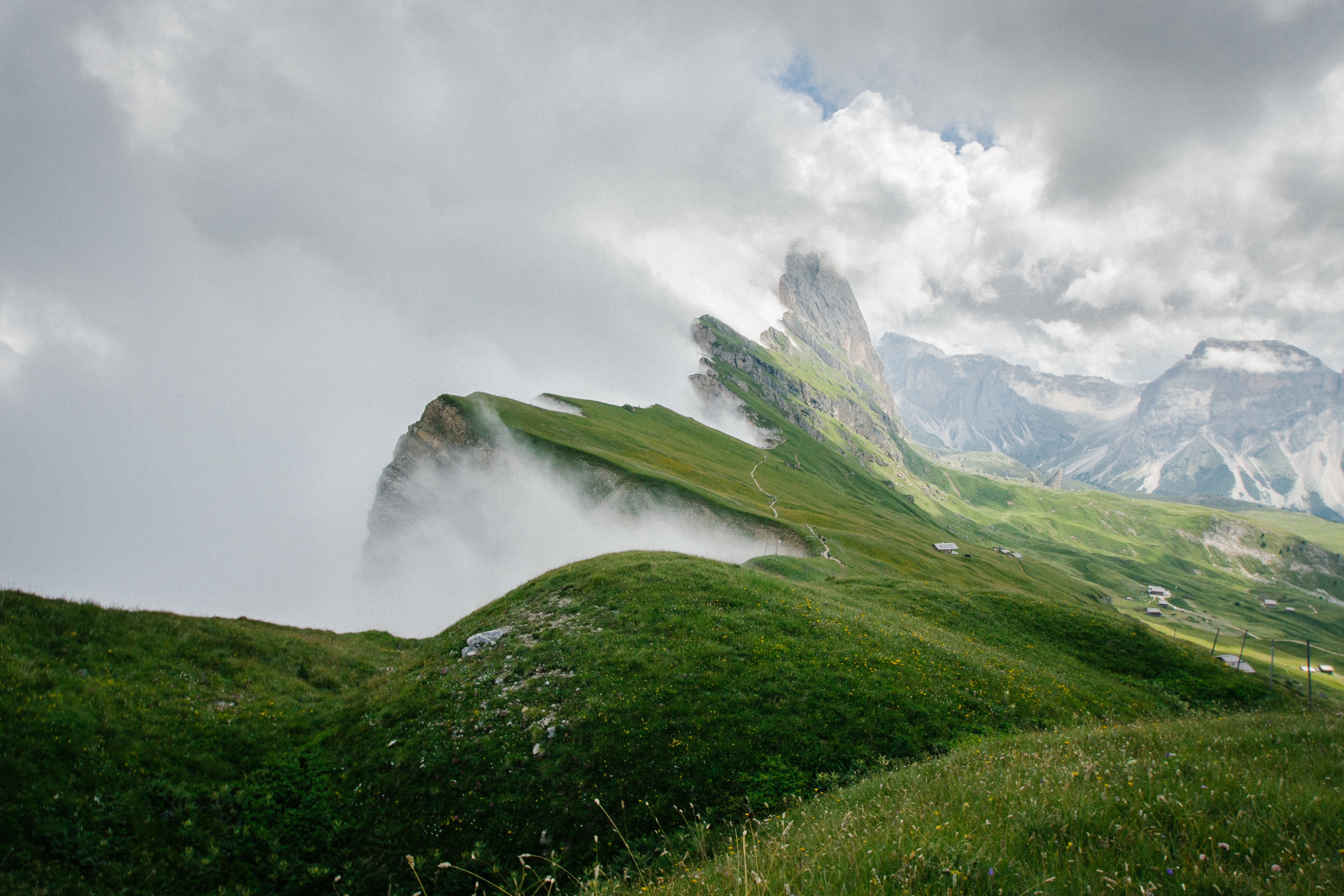 Sharp green mountain ridge with a narrow trail on the crest and thick white mist spilling over the cliff edge